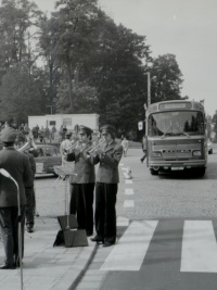 Eine uniformierte Musikgruppe spielt Blasinstrumente an einem Zebrastreifen, im Hintergrund steht ein Linienbus.